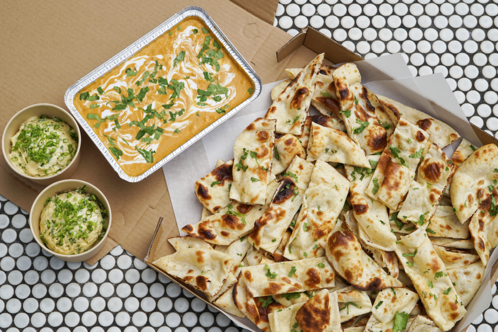 a box of freshly baked clay oven bread with a side of chickpea curry and scallion butter